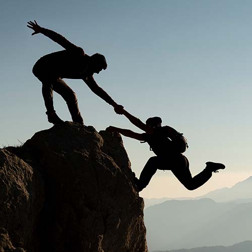 person on cliff helping another person climb